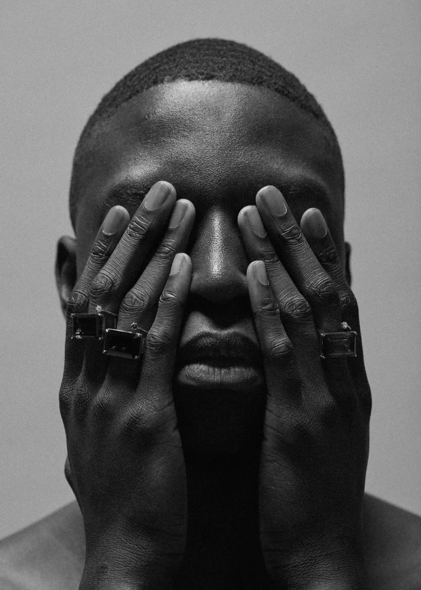 Black and white portrait of a man with hands covering his eyes.