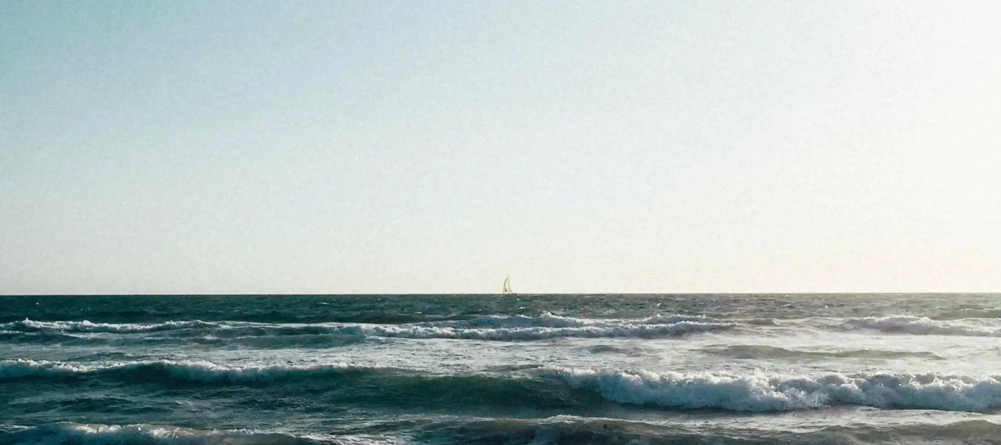 Wavy ocean with distant sailboat.