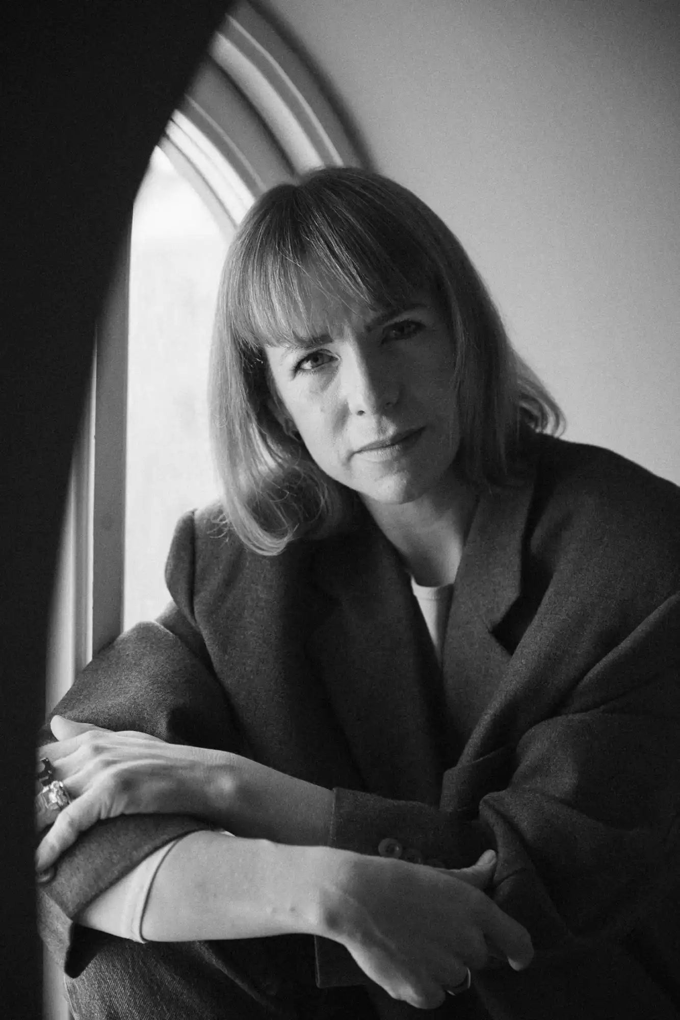 A woman with shoulder-length hair and bangs, wearing a blazer, with her arms crossed.